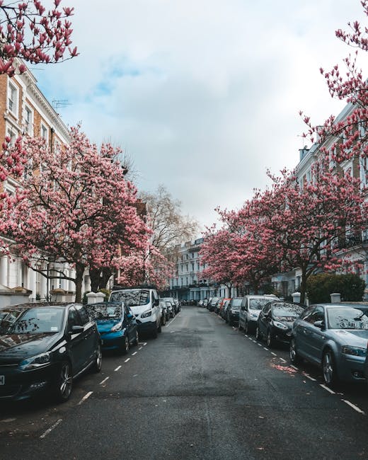 The image depicts a residential street in Kennington during spring, with a clear view down the road lined on both sides by parked cars, including a mix of sedans and hatchbacks. The street is bordered